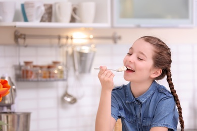 Photo of Cute girl eating tasty yogurt in kitchen