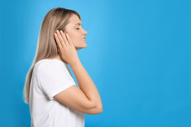 Young woman suffering from ear pain on light blue background. Space for text