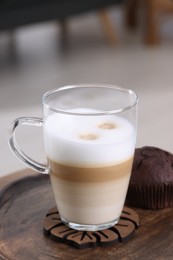 Photo of Cup of aromatic latte macchiato and chocolate muffin on table against blurred background