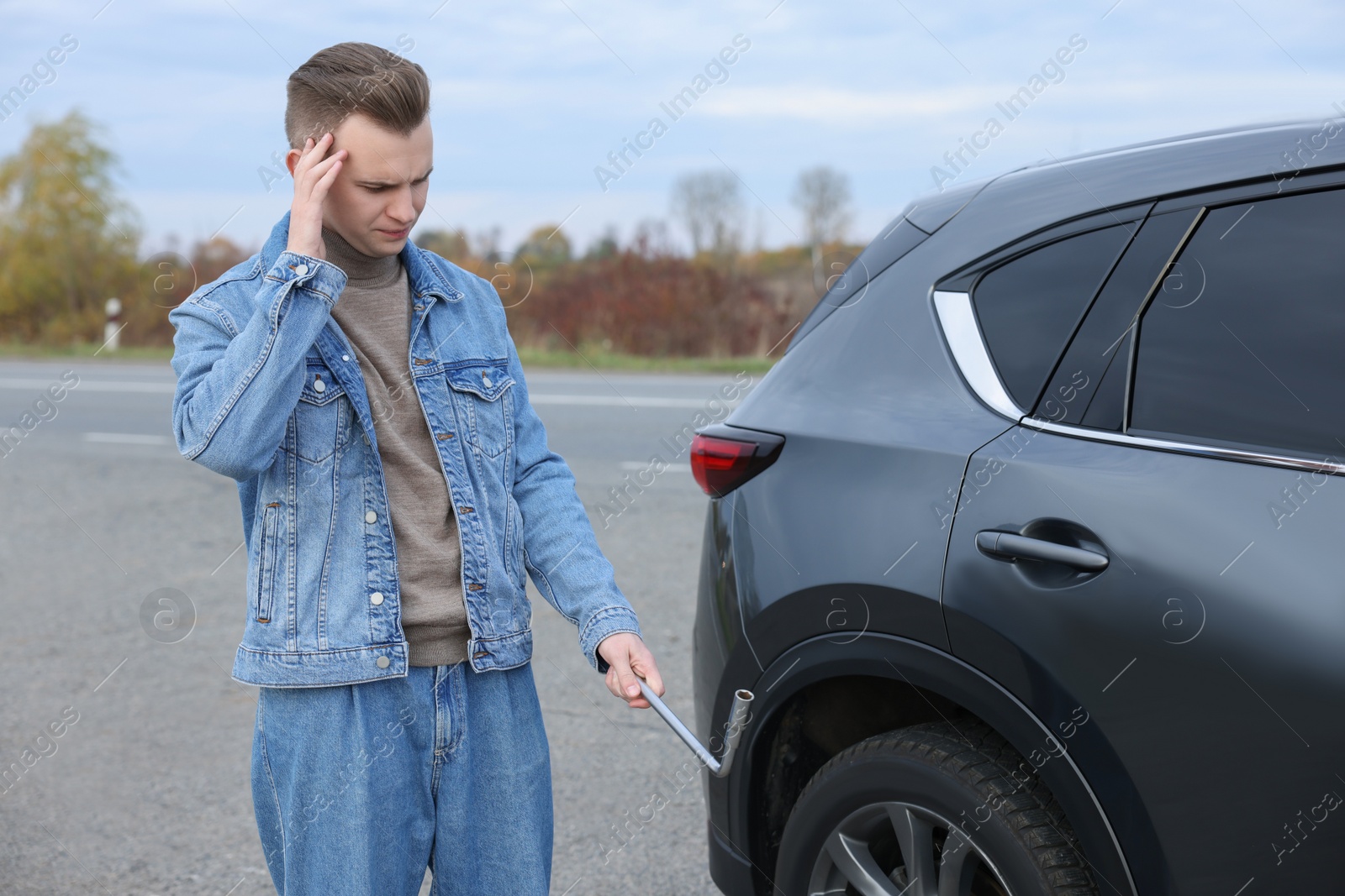 Photo of Worried young man near car with punctured wheel on roadside