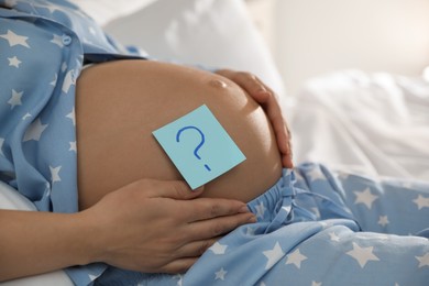 Photo of Pregnant woman with sticky note on belly indoors, closeup. Choosing baby name