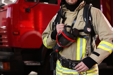 Photo of Firefighter in uniform with mask near red fire truck at station, closeup