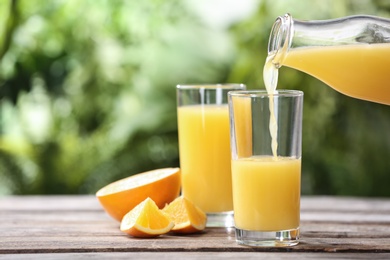 Pouring orange juice into glass on wooden table. Space for text