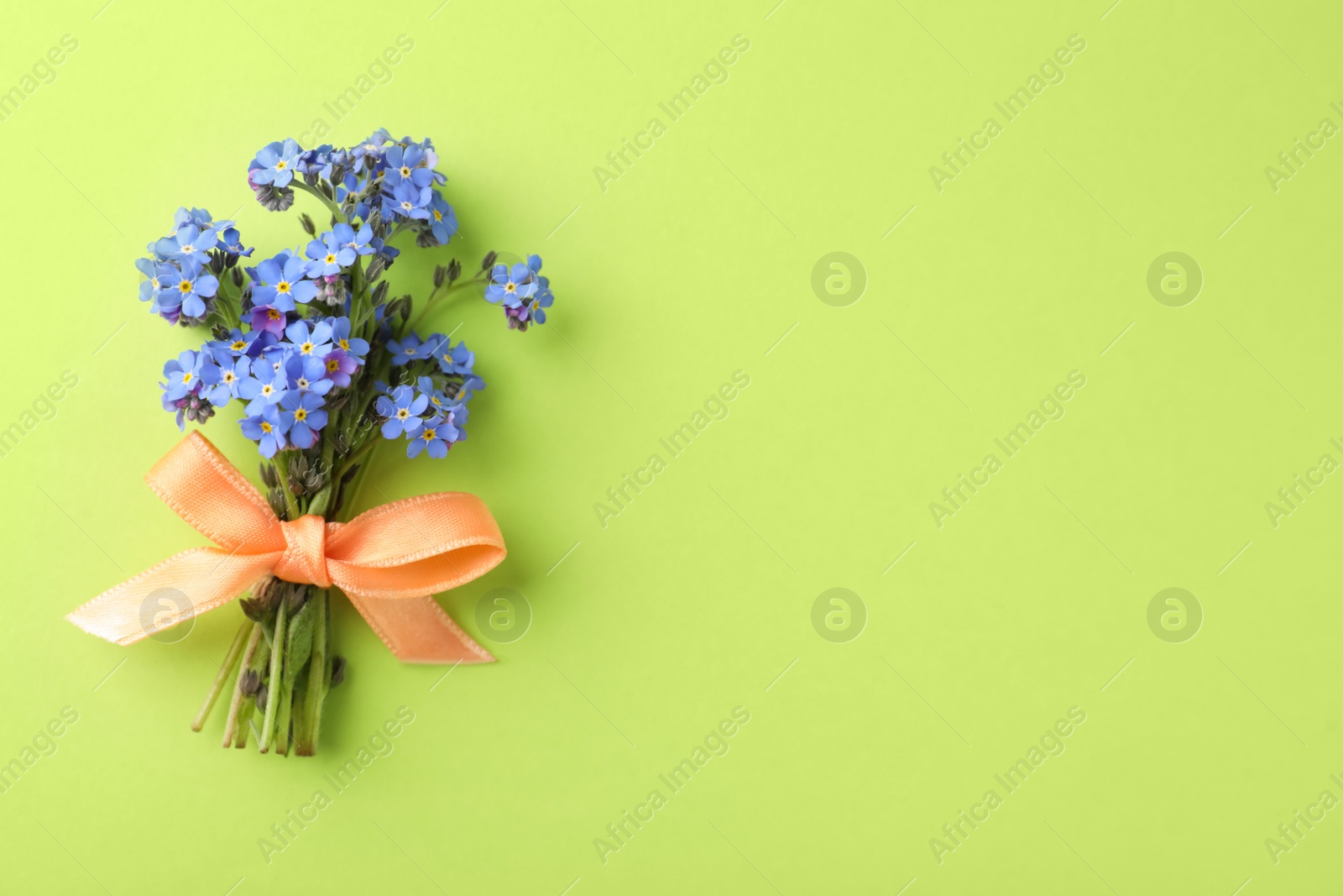 Photo of Beautiful blue forget-me-not flowers tied with ribbon on light green background, top view. Space for text
