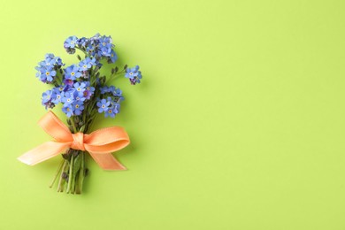 Beautiful blue forget-me-not flowers tied with ribbon on light green background, top view. Space for text