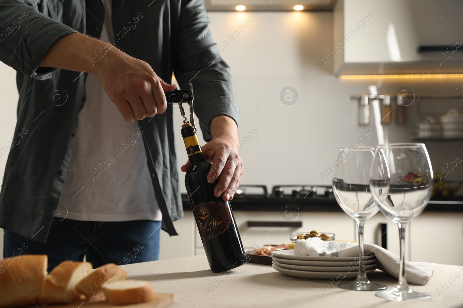 Photo of Man opening wine bottle with corkscrew at table indoors, closeup