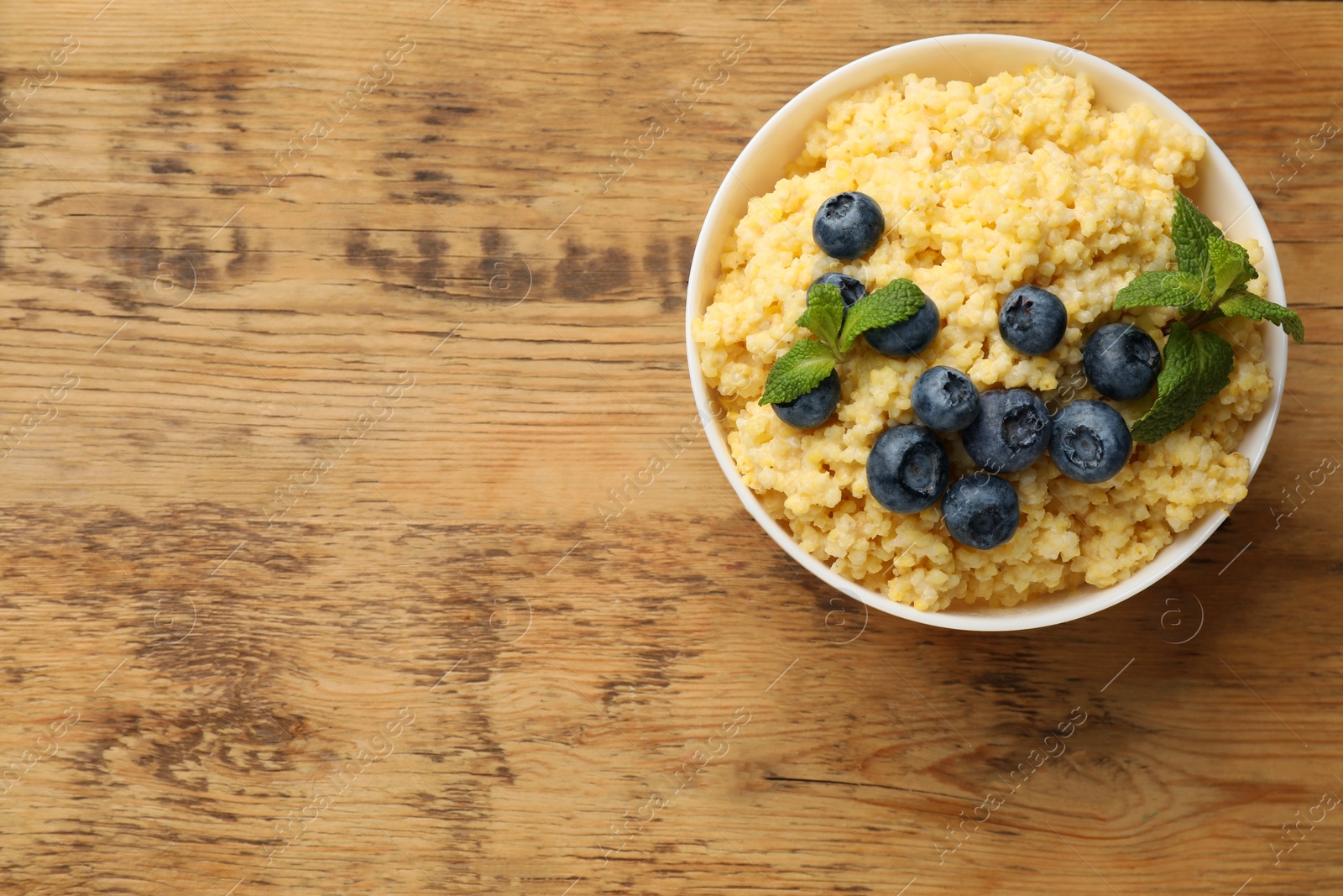 Photo of Tasty millet porridge with blueberries and mint in bowl on wooden table, top view. Space for text