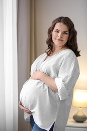 Photo of Young pregnant woman in casual clothes at home