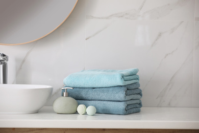 Photo of Stack of fresh towels, soap dispenser and bath bombs on countertop  indoors
