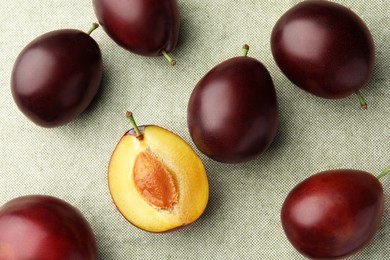 Photo of Many tasty ripe plums on light fabric, flat lay