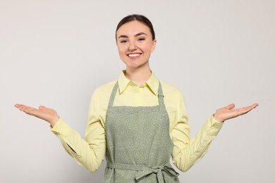 Beautiful young woman in clean apron with pattern on light grey background