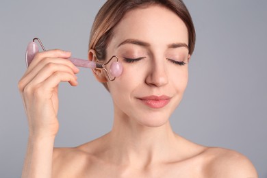 Photo of Young woman using natural rose quartz face roller on light grey background