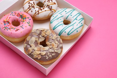 Photo of Box with different tasty glazed donuts on pink background, closeup