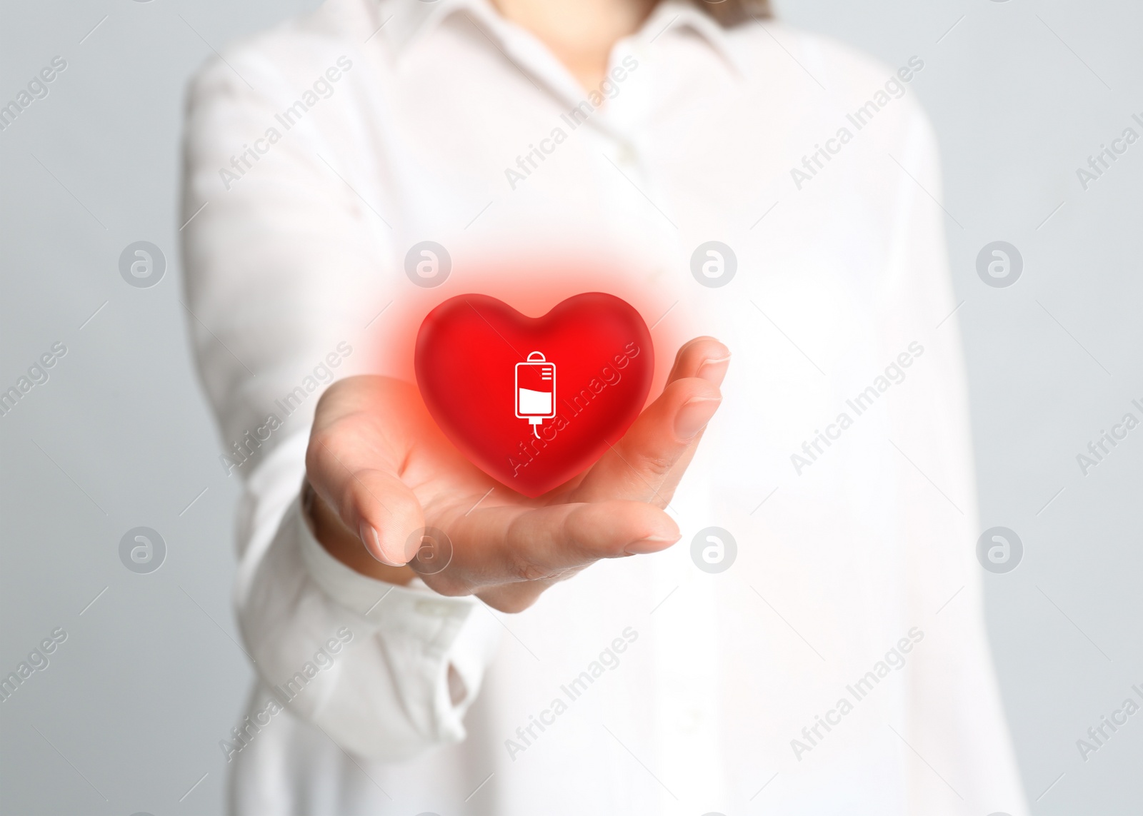 Image of Woman holding red heart in hand on light grey background, closeup. Blood donation concept