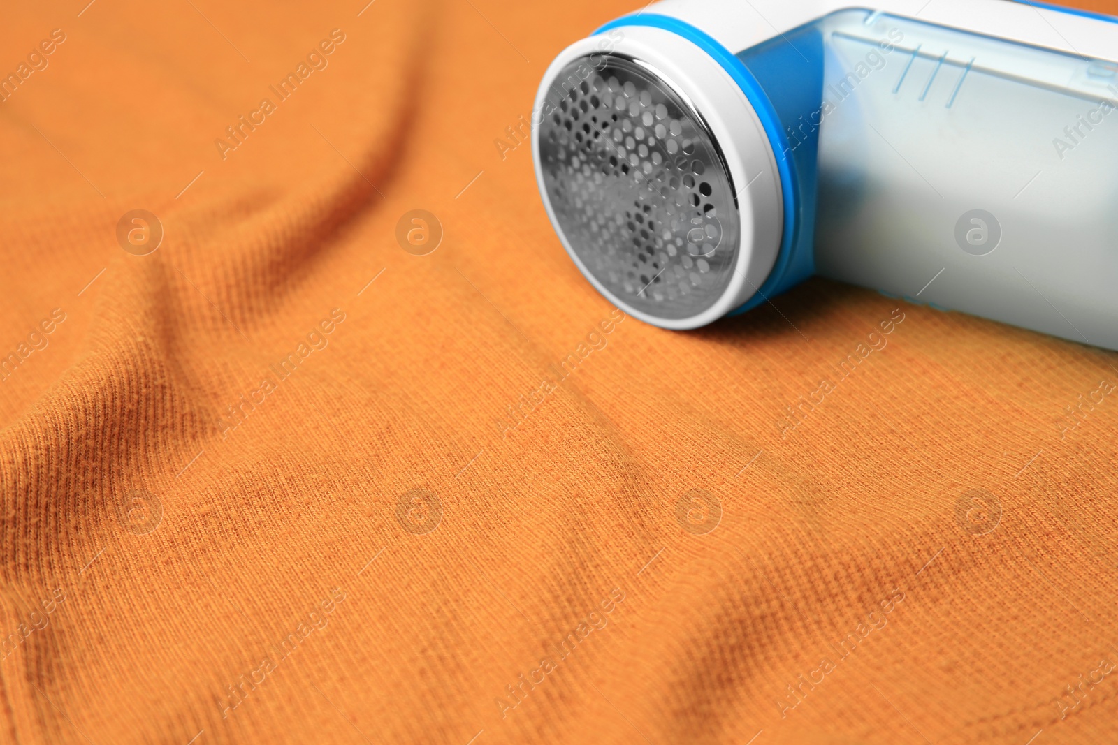 Photo of Modern fabric shaver on orange cloth with lint, closeup. Space for text