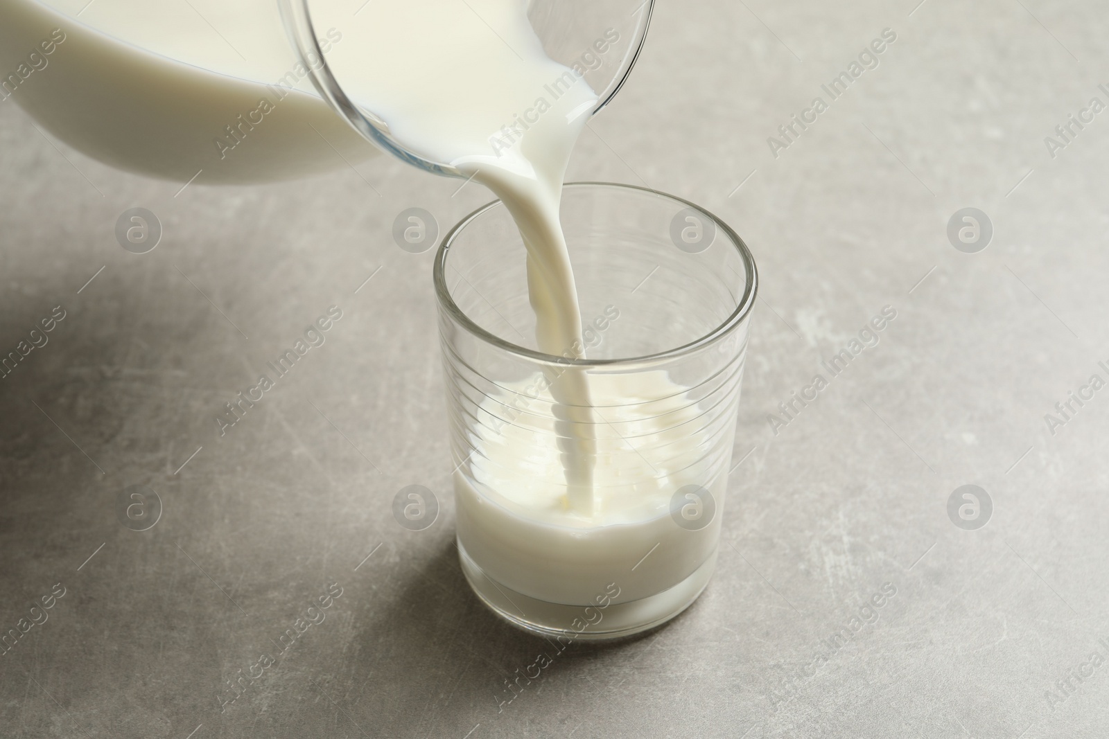 Photo of Pouring milk into glass on grey table