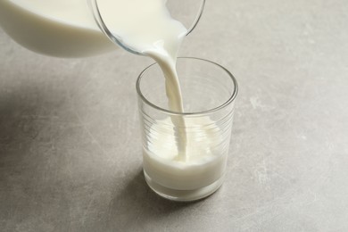 Photo of Pouring milk into glass on grey table