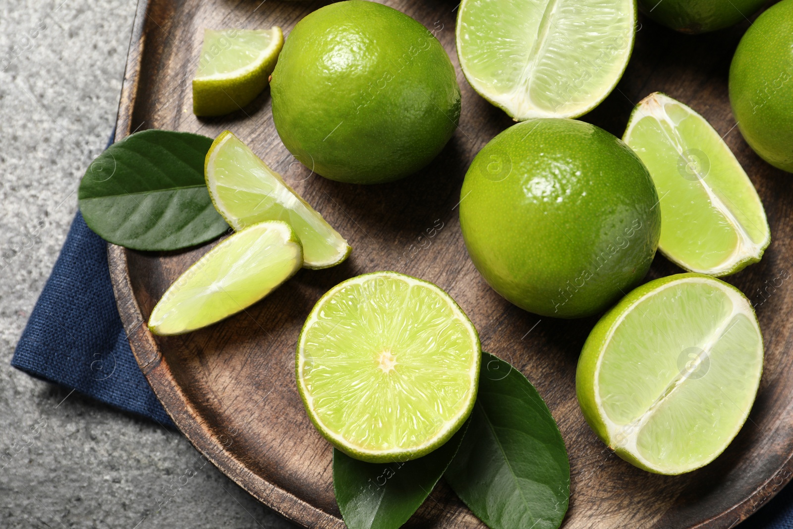 Photo of Fresh ripe limes and leaves on grey table, top view