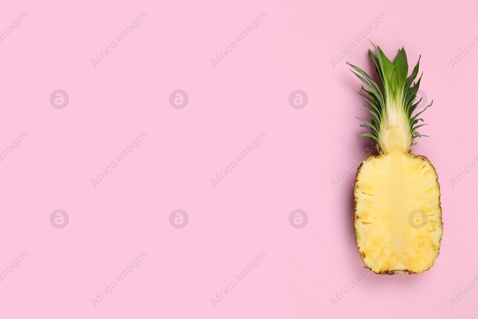 Photo of Half of ripe pineapple on pale pink background, top view. Space for text