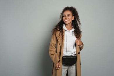 Photo of Beautiful African American woman with stylish waist bag on grey background, space for text