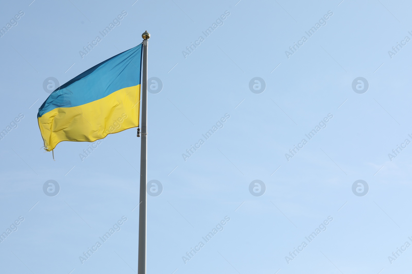 Photo of Flag of Ukraine waving on pole against blue sky. Space for text