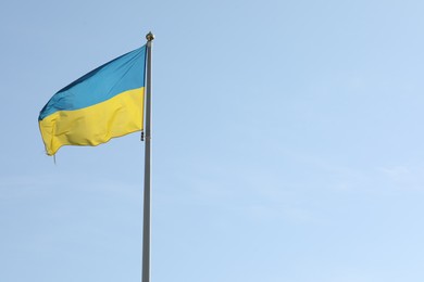 Photo of Flag of Ukraine waving on pole against blue sky. Space for text