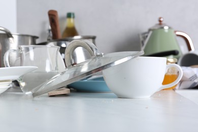 Many dirty utensils and dishware on countertop in messy kitchen, closeup