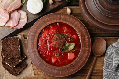 Stylish brown clay plate with Ukrainian borsch served on wooden table, flat lay