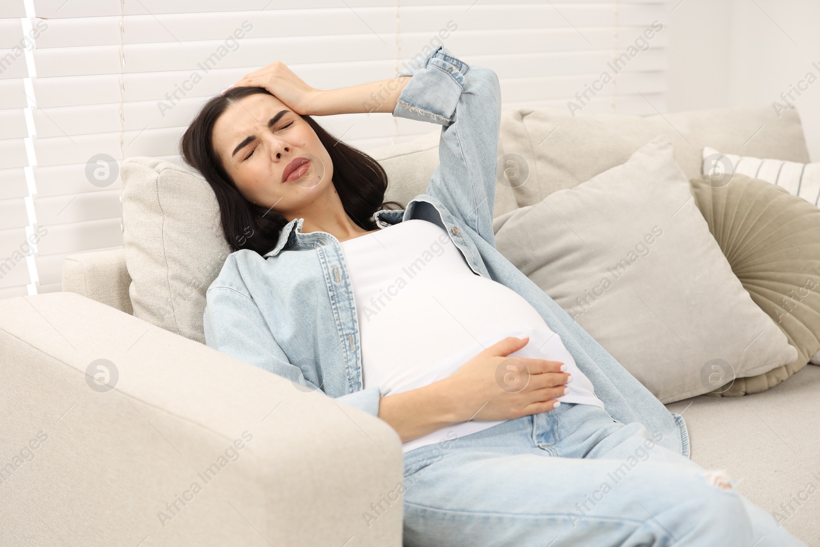 Photo of Pregnant woman suffering from headache on sofa at home