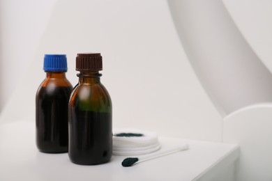 Bottles of brilliant green, cotton bud and pads on white table indoors. Space for text