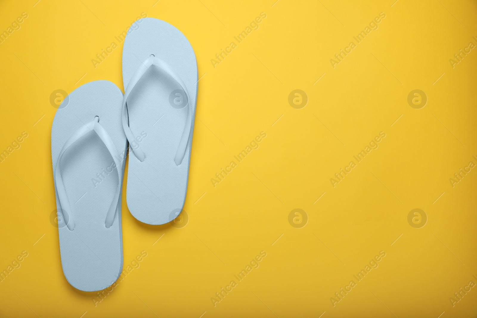 Photo of Stylish white flip flops on yellow background, top view. Space for text