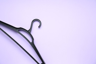 Empty black hanger on lilac background, top view. Space for text