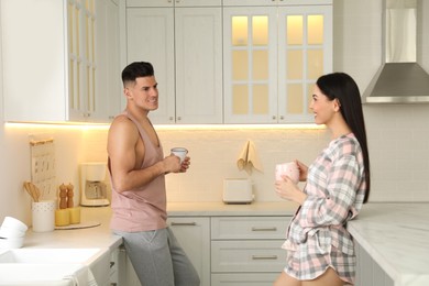 Happy couple wearing pyjamas with cups of coffee in kitchen