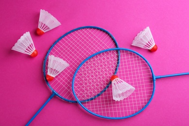 Photo of Badminton rackets and shuttlecocks on pink background, flat lay
