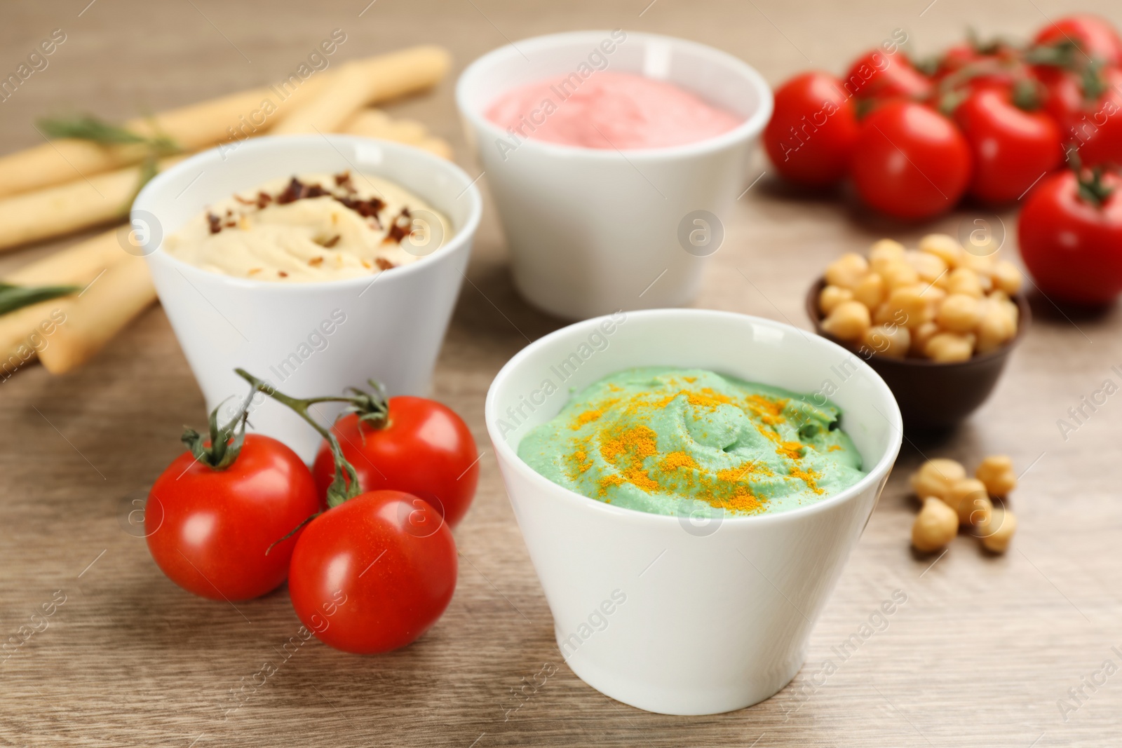 Photo of Different kinds of tasty hummus with ingredients on wooden table