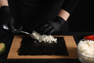 Photo of Chef in gloves making sushi roll at dark table, closeup