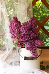 Photo of Beautiful lilac flowers in milk can near window indoors