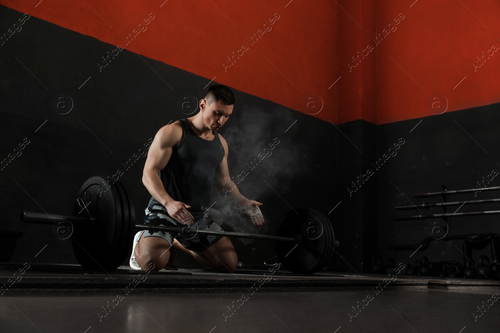 Photo of Strong man applying magnesium powder on hands before training with barbell in gym