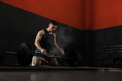 Photo of Strong man applying magnesium powder on hands before training with barbell in gym