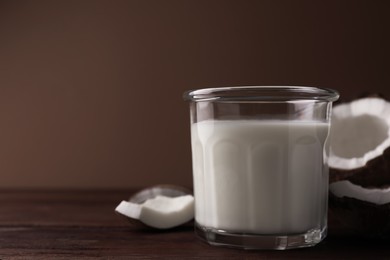 Photo of Glass of delicious vegan milk and coconut pieces on wooden table, space for text