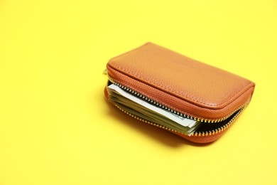 Photo of Stylish brown leather purse with banknotes on yellow background. Space for text