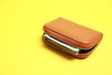 Stylish brown leather purse with banknotes on yellow background. Space for text