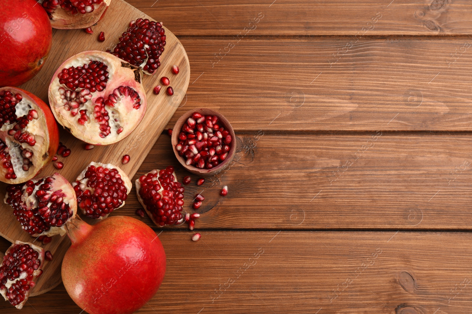 Photo of Delicious ripe pomegranates on wooden table, flat lay. Space for text