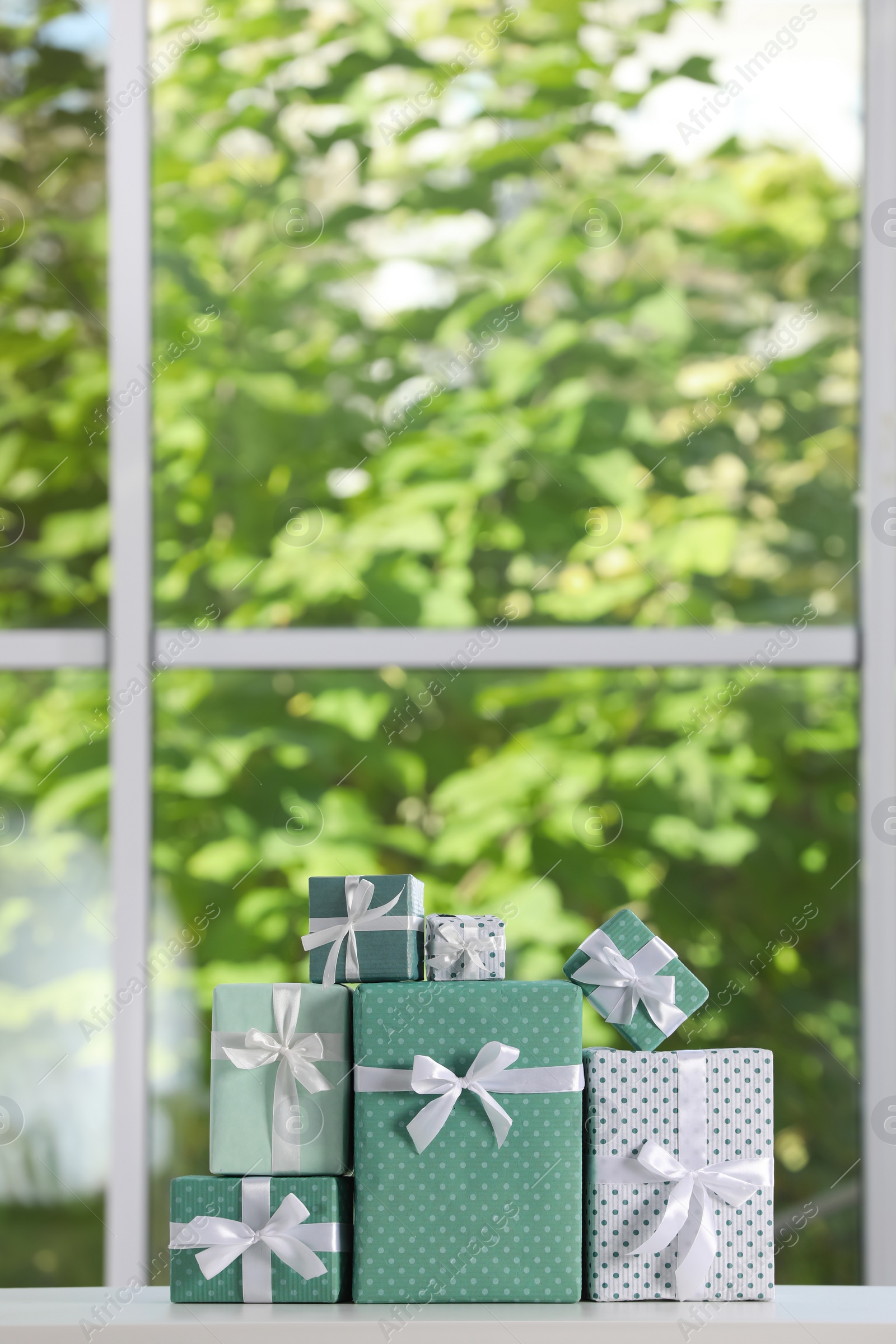 Photo of Stack of beautifully wrapped gift boxes on white table  near window. Space for text