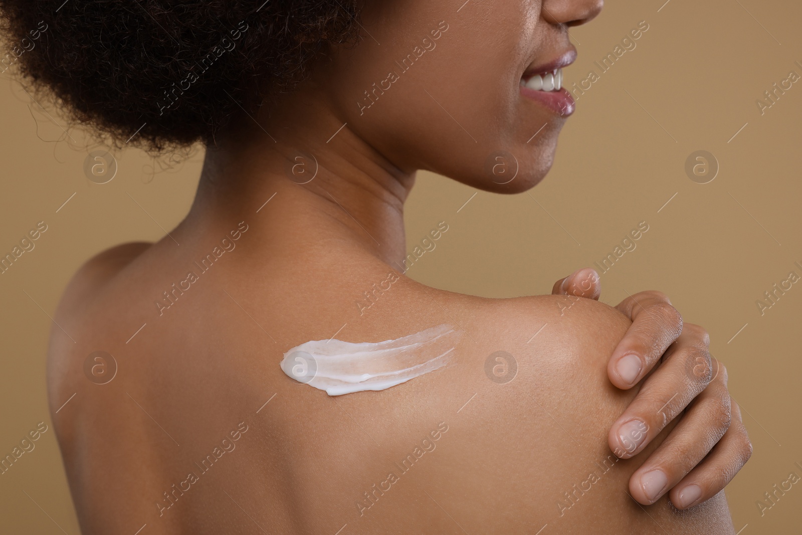 Photo of Young woman applying body cream onto back on beige background, closeup