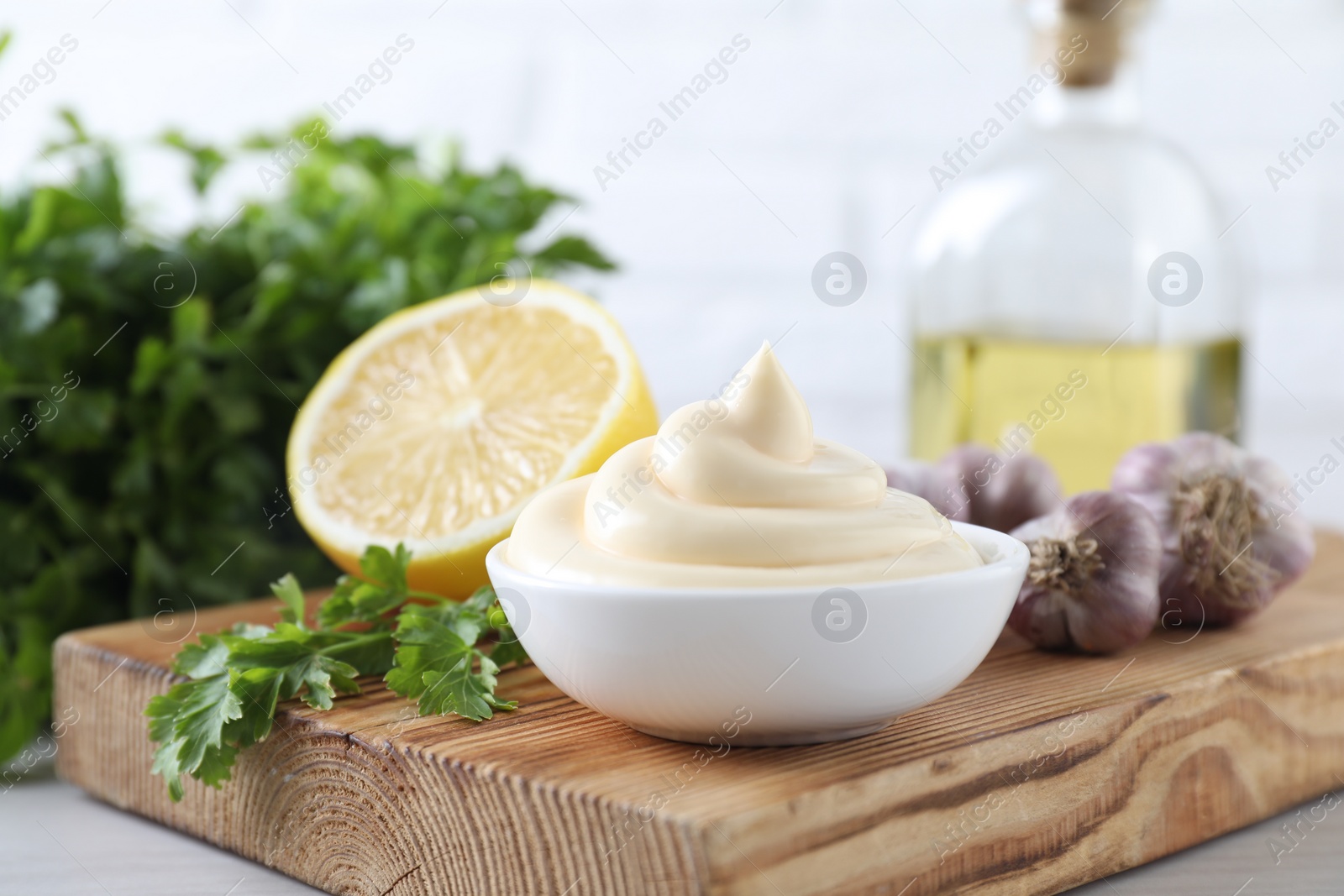 Photo of Tasty mayonnaise sauce in bowl, parsley, garlic and lemon on table, closeup