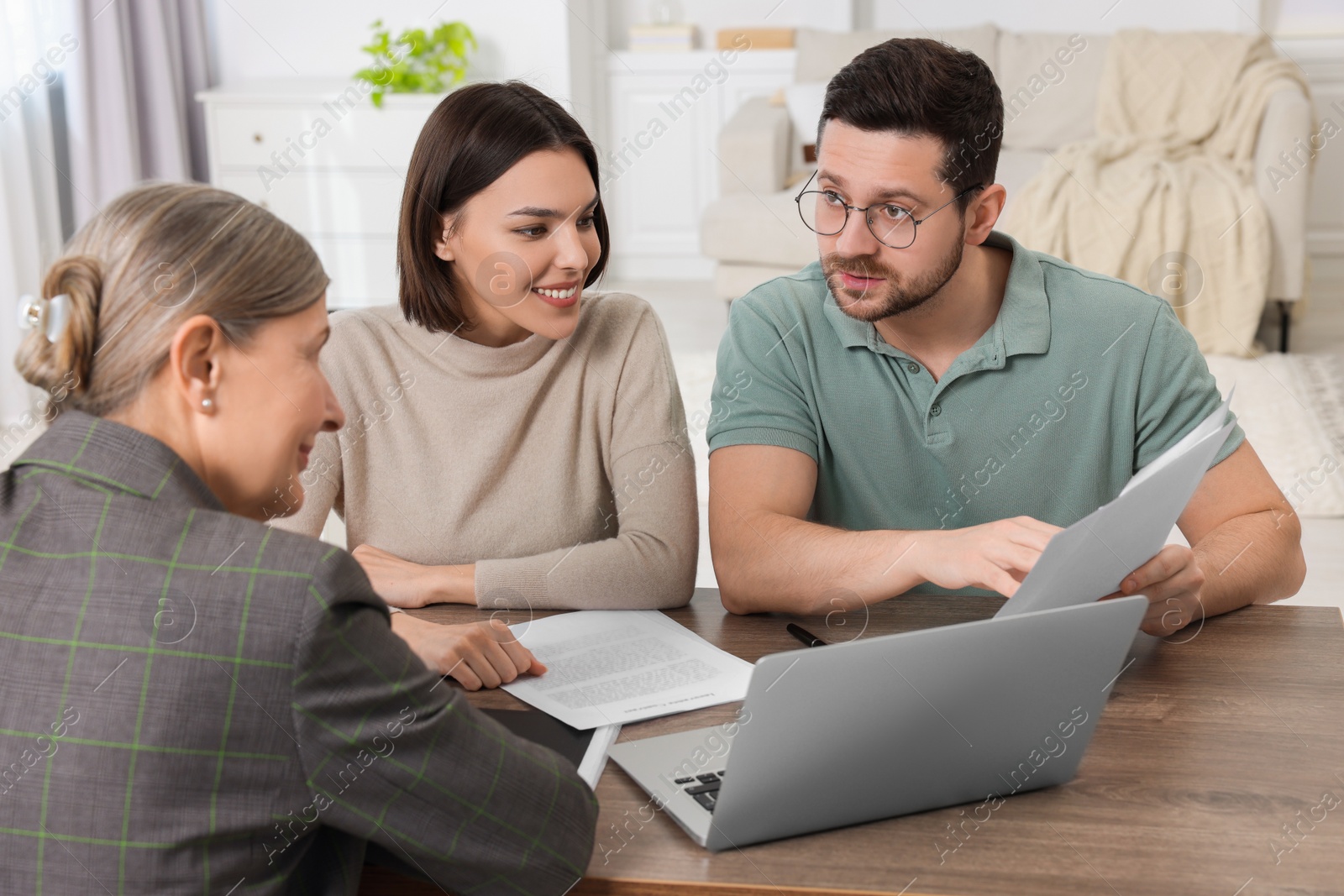 Photo of Young couple consulting insurance agent about pension plan at wooden table indoors