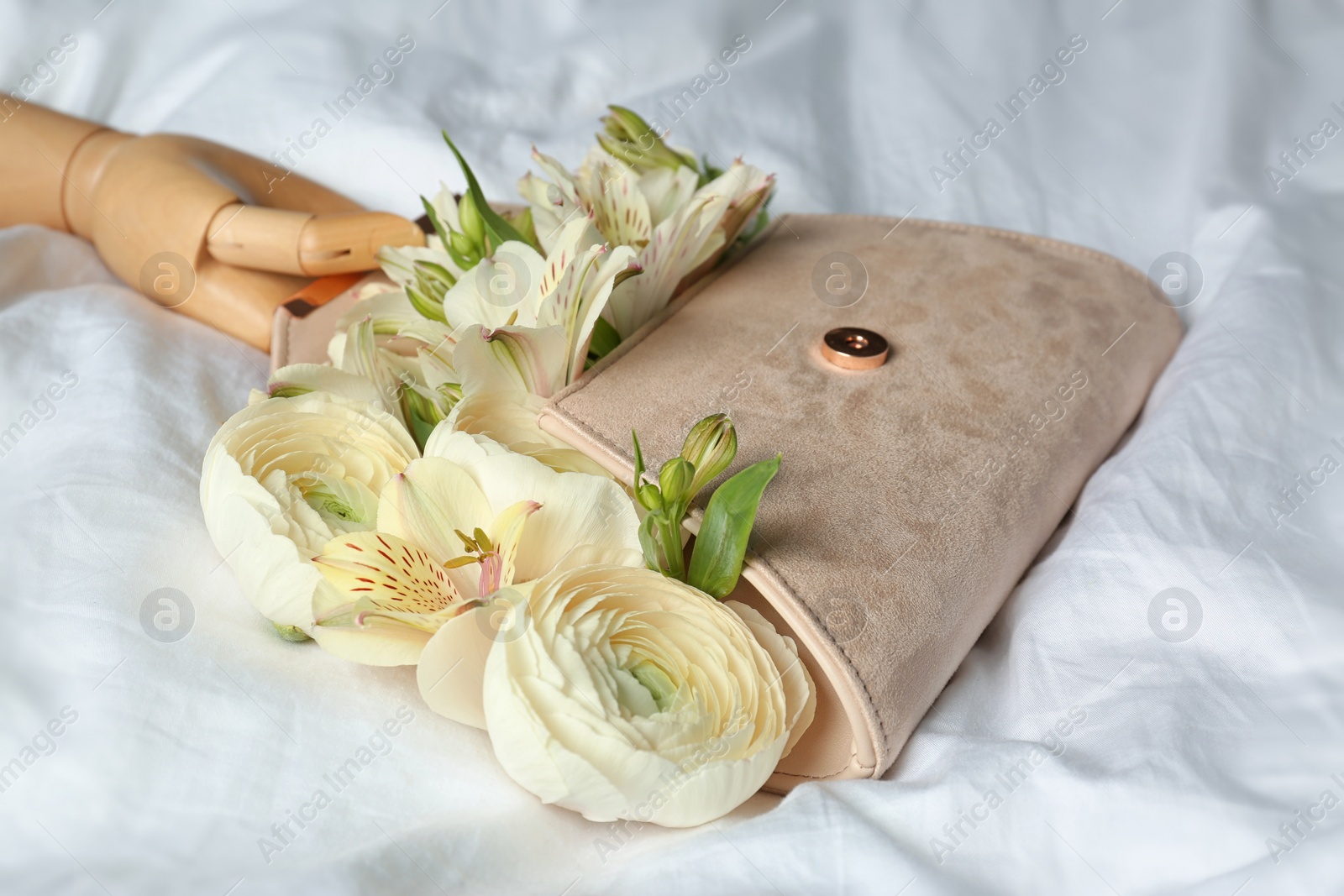 Photo of Stylish clutch with spring flowers and wooden mannequin hand on crumpled sheet