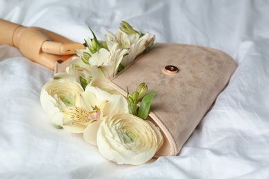 Photo of Stylish clutch with spring flowers and wooden mannequin hand on crumpled sheet