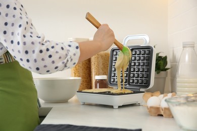 Woman pouring dough onto Belgian waffle maker in kitchen, closeup